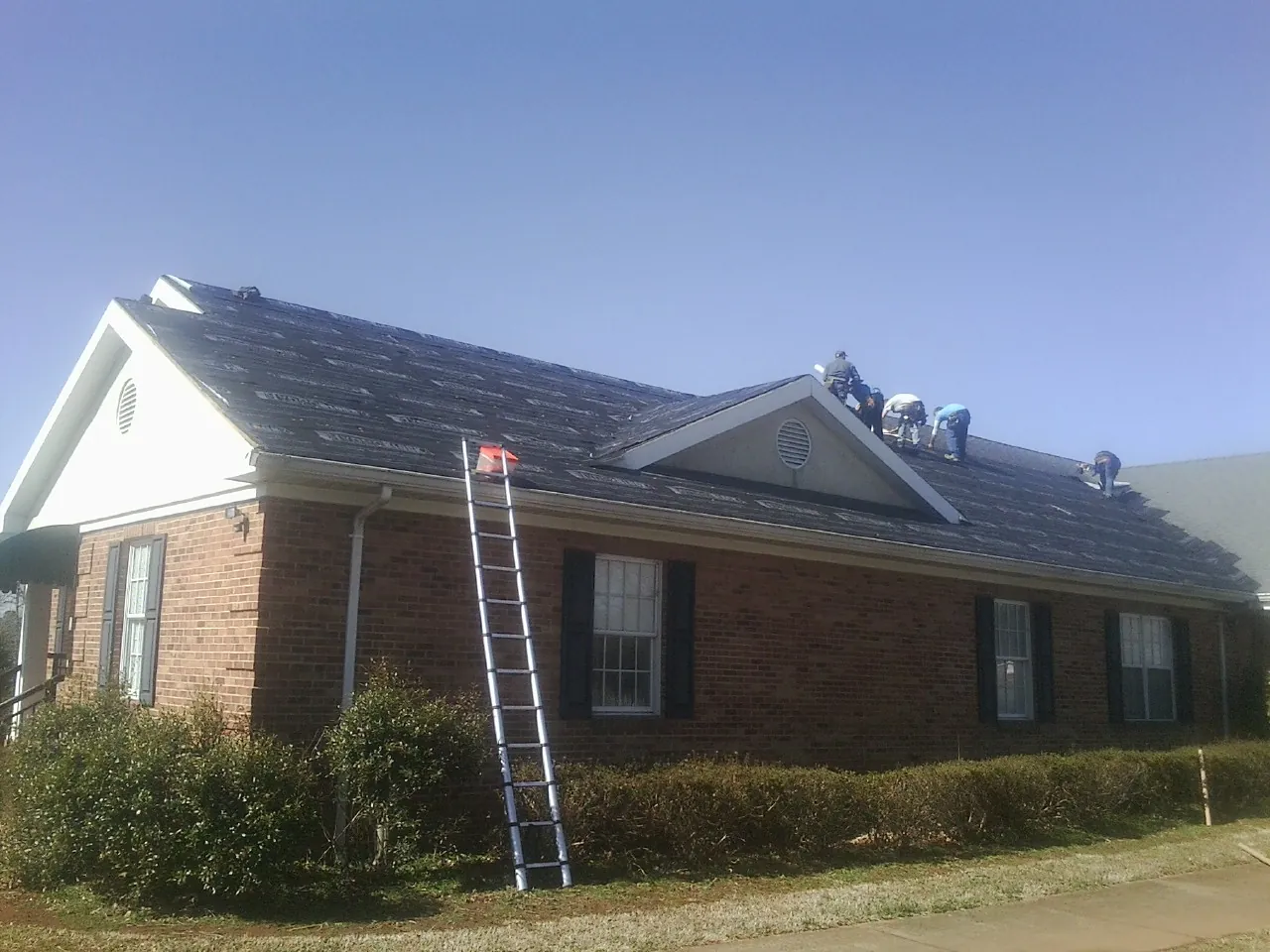 Crew tearing shingles off a brick ranch roof with a ladder set — Metal Roof Repair work by our crew in Lake Hiawatha