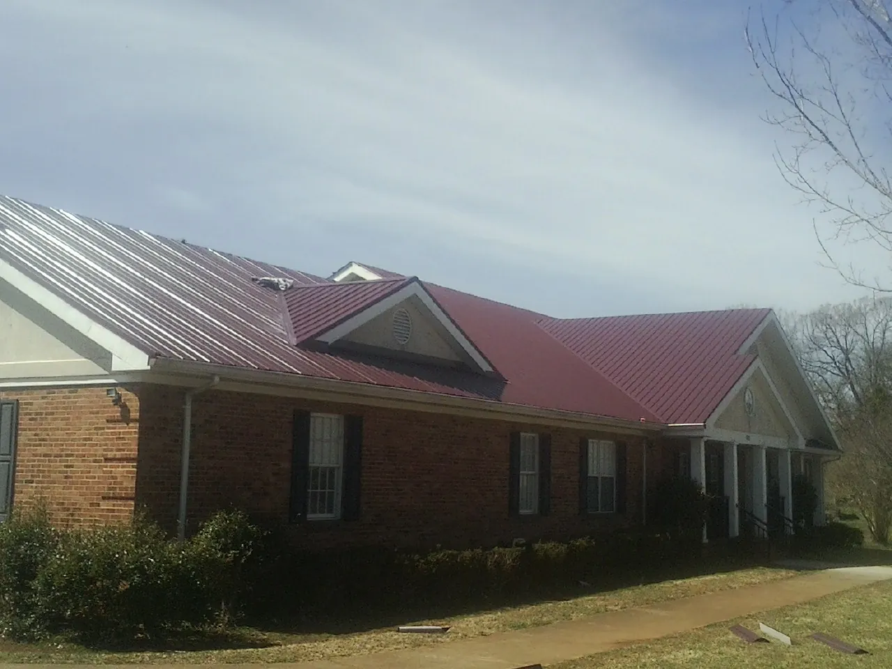Red metal roof with gabled entries on a long brick building, from a Hail Damage Roof Repair job in Lake Hiawatha