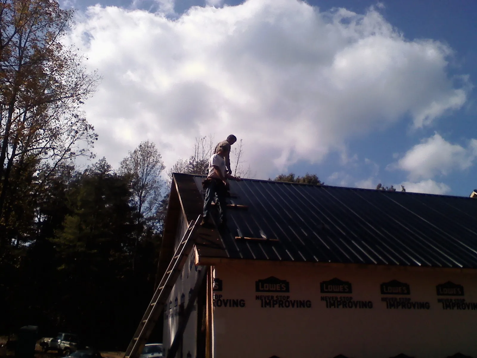 Roofer fastening dark metal panels high against a cloudy sky, from a Roof Inspection job in Lake Hiawatha