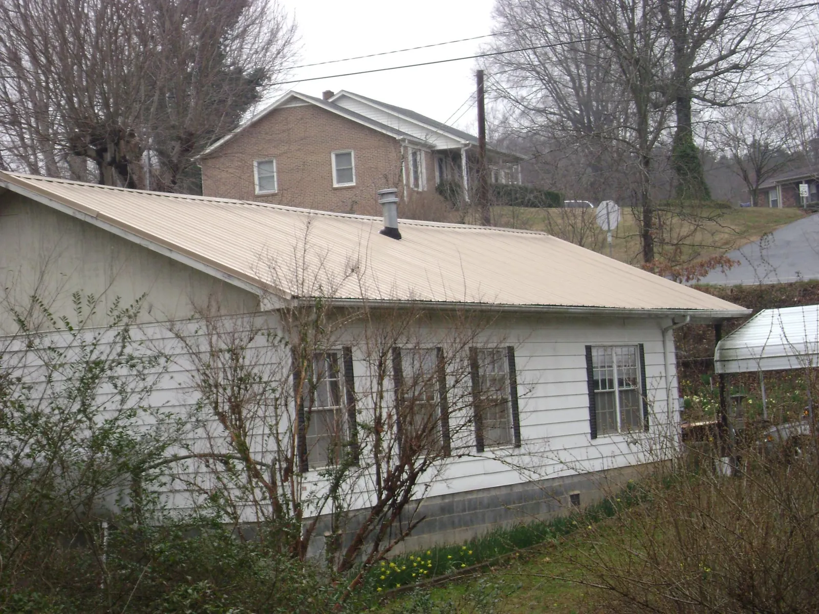 Tan metal roof on a white sided house set into a hillside — Commercial Roofing by Roofing Brothers in Lake Hiawatha